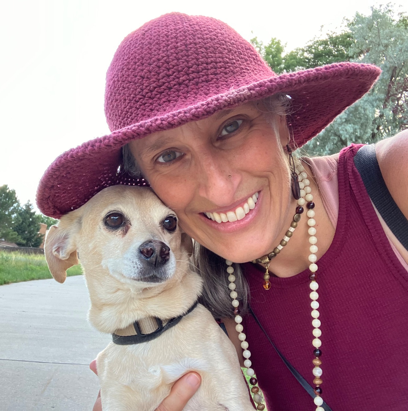 Connie in a raspberry crocheted sun hat holding Sami close, cheek to cheek, on a summer trail