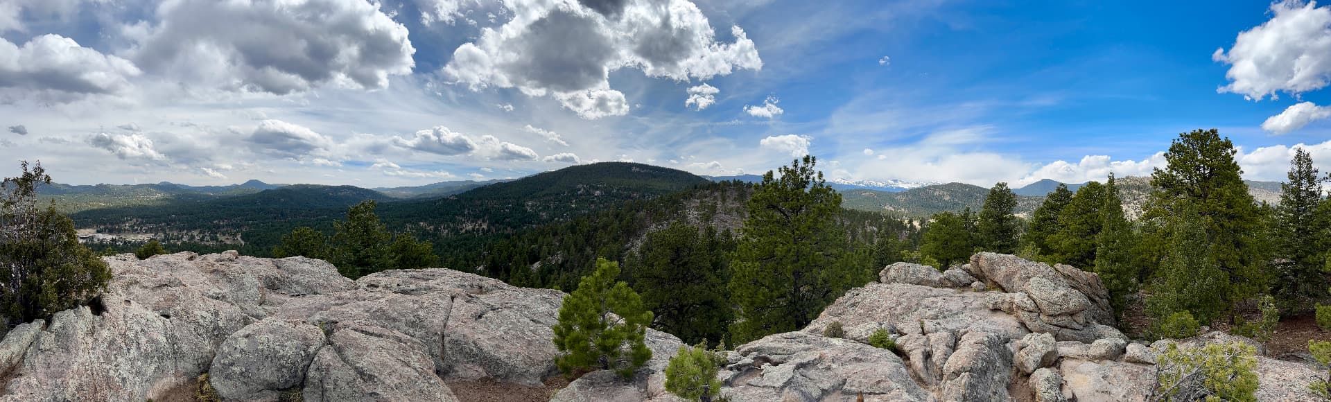 Panoramic view of forested Colorado foothills and granite outcrops under a wide cloudy sky